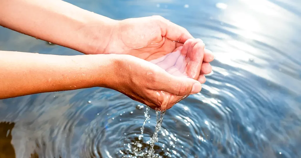 Woman taking clear water at a lake by hands