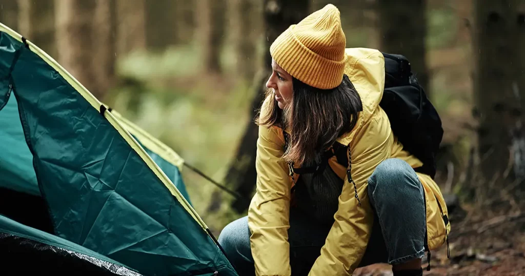 Young woman in outdoor gear setting up her tent in a clearing after a day hiking in the woods