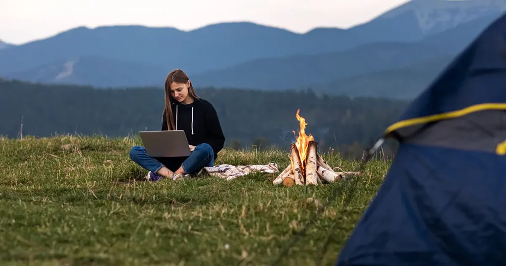 young female freelancer working on laptop in the mountains in the evening