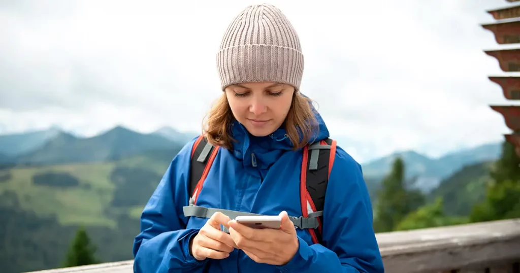 Woman with backpack standing and using cell phone in mountains