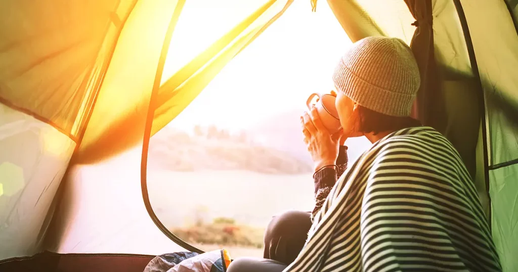 Morning in temt camp.Woman with cup of hot tea sit in camping tent