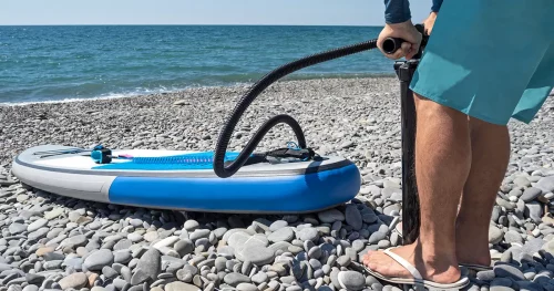 Man inflating stand up paddle board with manual pump at sea background