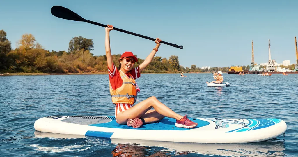 Joyful smiling woman sitting on an inflatable sup board with raised up paddle