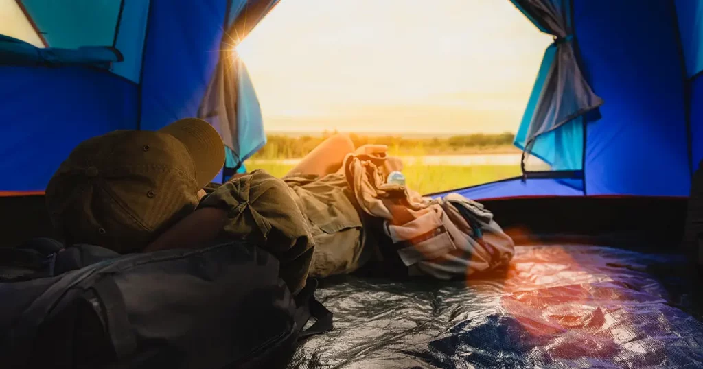 Young woman lying in tent or sleeping on bag with a sunset view on mountains and lake