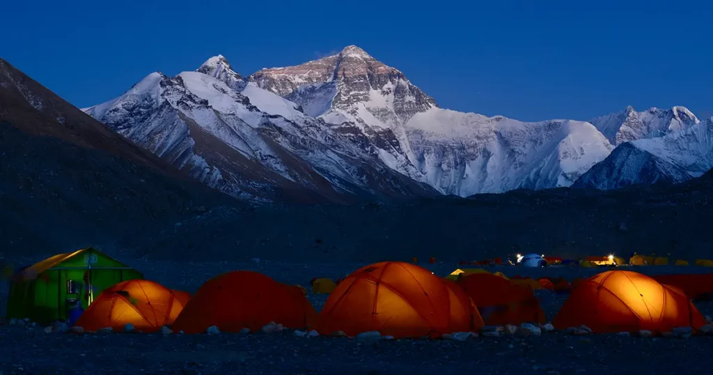 orange tents in base camp glow as the sun sets over the north face of Mount Everest