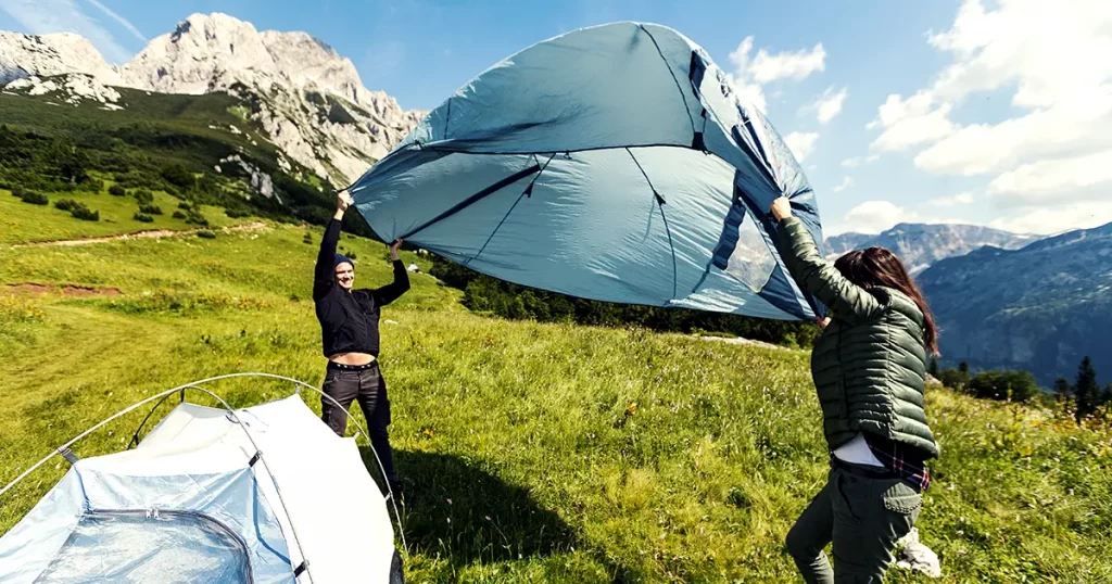 Couple of hikers setting up a camping tent on the mountain