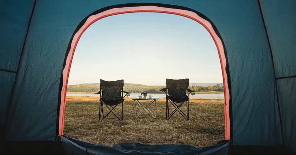 View from inside tent, Outdoor two empty chairs with picnic table and moka pot coffee for Camping.