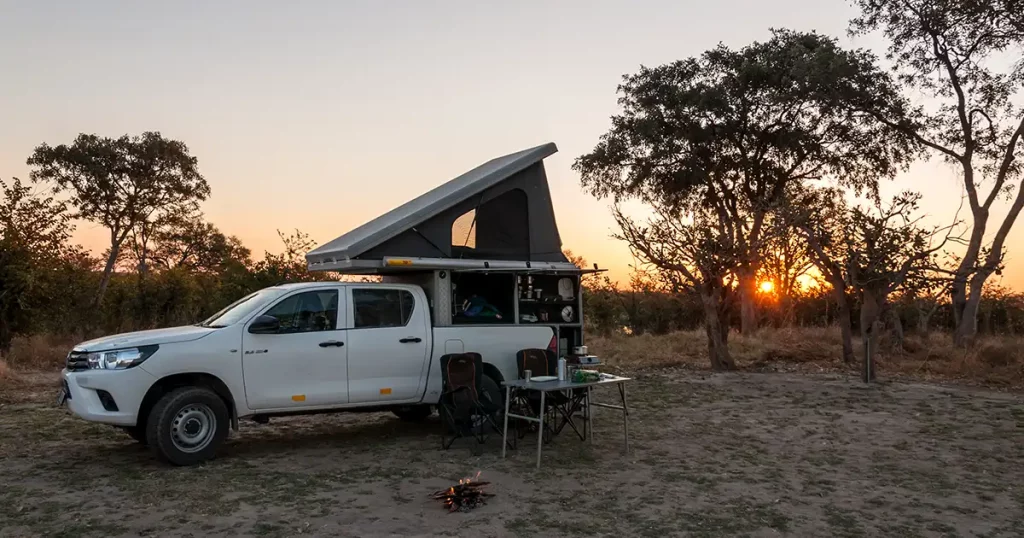 car with a rooftop tent parked in a bush campsite while the sun sets over the savannah