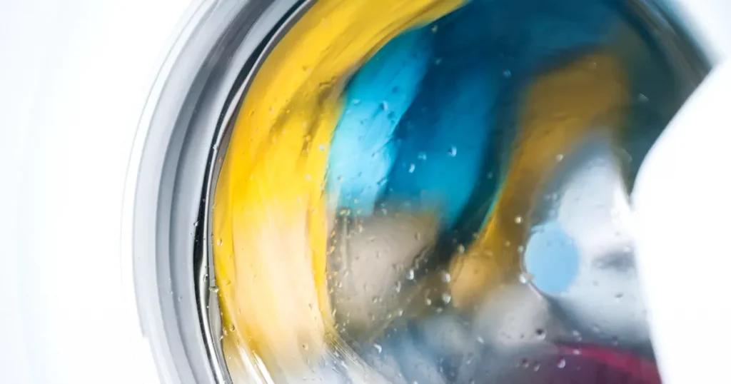 Process of cleaning color cloth in washing machine, stainless drum inside with wet towels, closeup, nobody