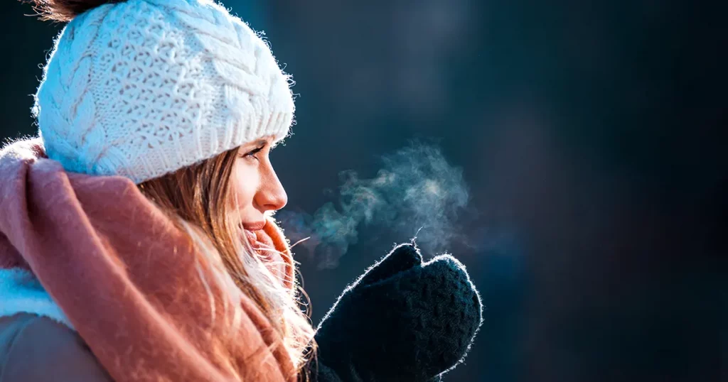 Woman breathing on her hands to keep them warm at cold winter day