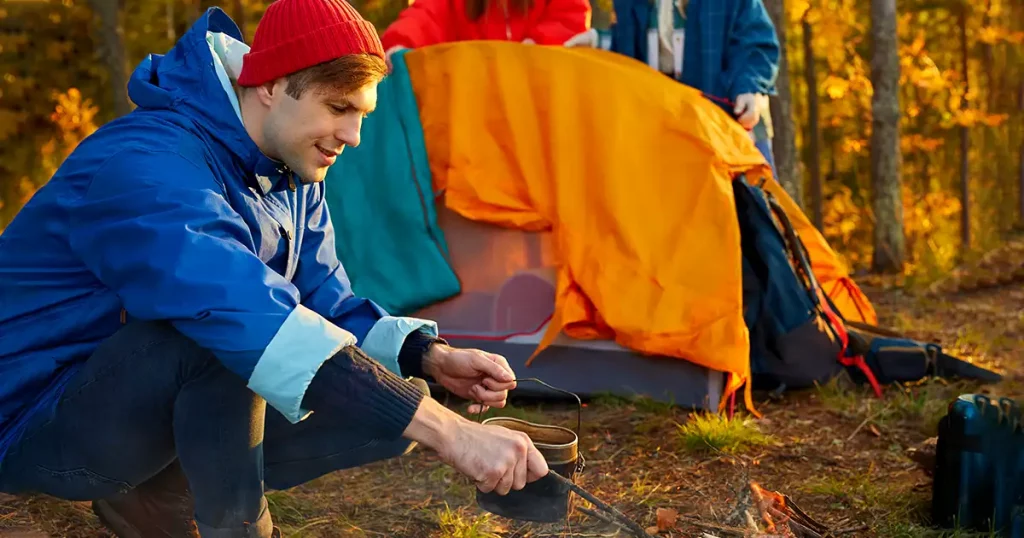 man trying to light a fire during a trip in mountains, keep warm after a long hike