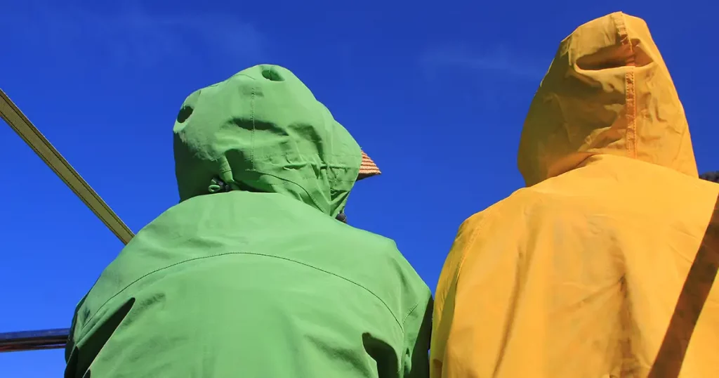 two adults wearing bright yellow and green raincoats against a bright blue sky