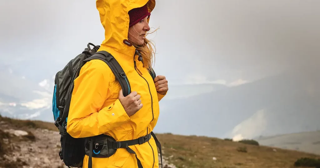 Woman hiking at mountains in extreme weather. Tourist wearing waterproof jacket with hood. Sports clothing and backpack