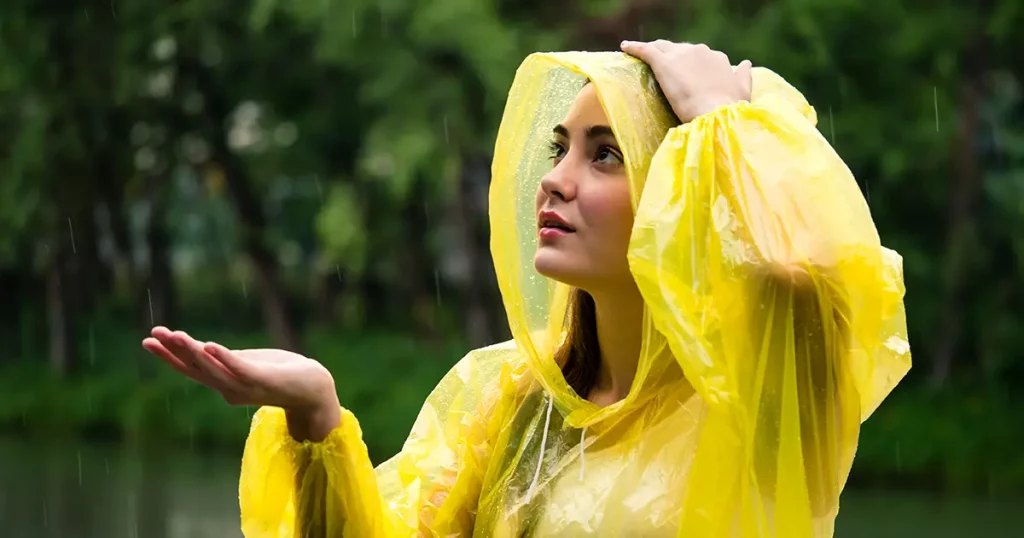 Young beautiful happy woman in yellow raincoat enjoying the rain