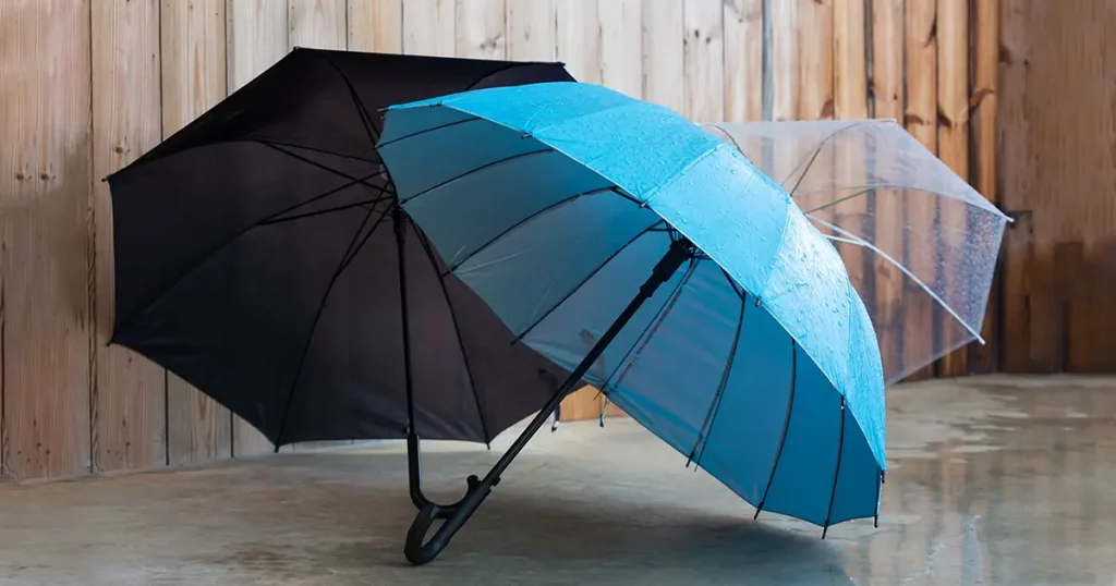 Umbrellas on a concrete floor in front of a wooden home in a rainy day.