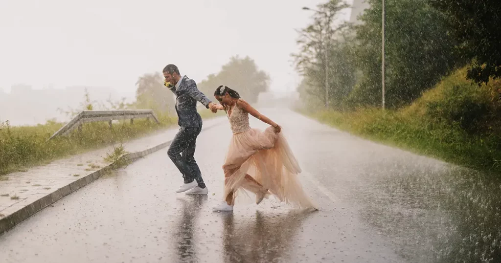 Silly young just married couple crossing road on rainy day. Running in wet ceremonial clothes.