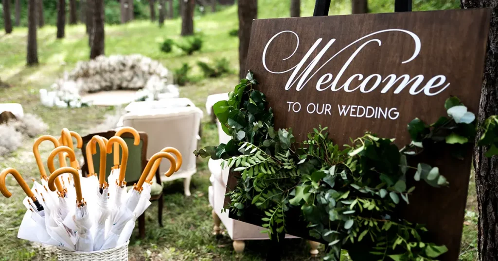 decor. Outdoor wooden welcome board decorated with green branches, basket with umbrellas in case of rain