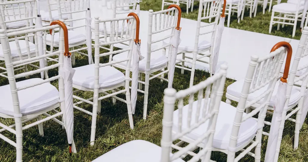 white chairs stand on green grass in the area of the wedding ceremony, white umbrellas are hanging on the chairs