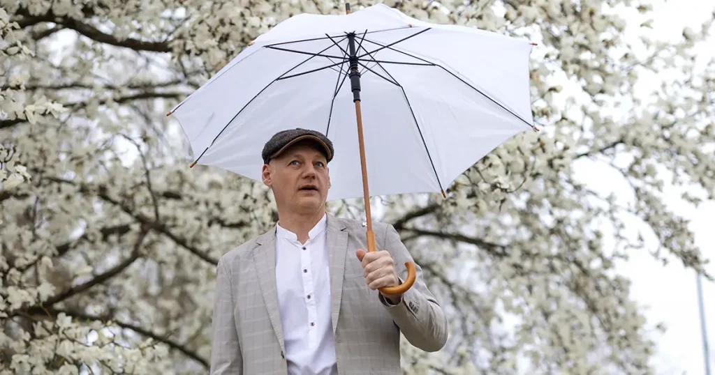 Beautiful smiling man with umbrella amid white flowering magnolia