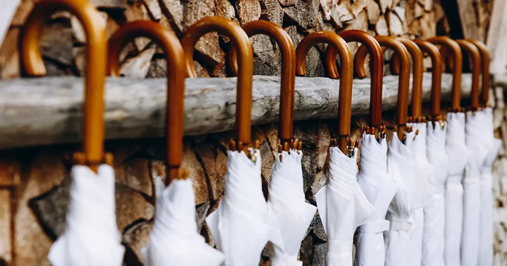Close up of white closed umbrellas with wooden handle prepared for wedding guests by organizers