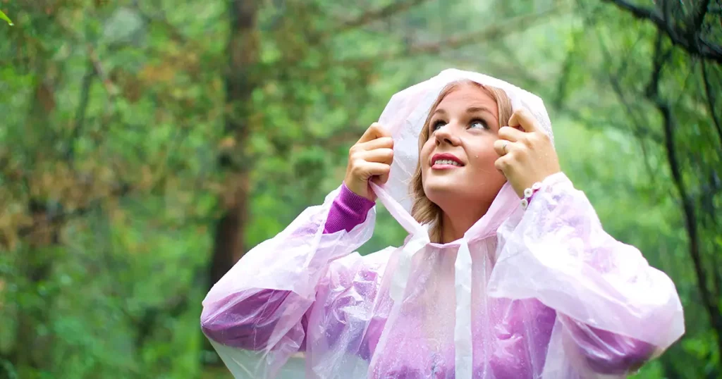 Beautiful woman in plastic rain poncho in forest looking up