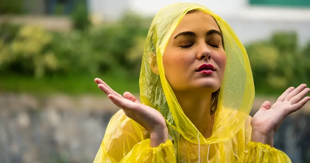 Young beautiful happy woman in yellow raincoat enjoying the rain