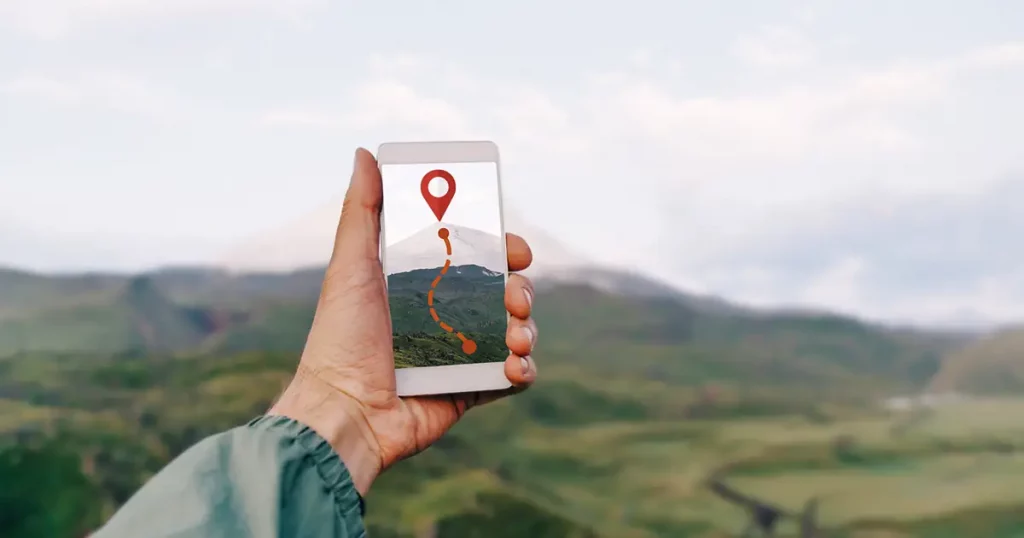 Traveler hiker man holding smartphone in a hand and using GPS app with trekking in summer mountains outdoor. Point of view in first person