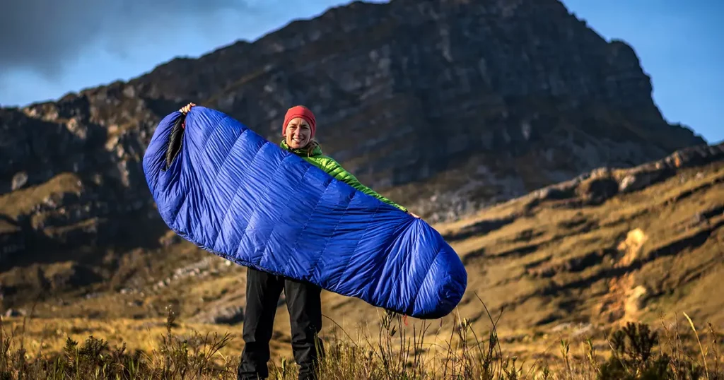 Young outdoor sporty woman posing with sleeping bag in high mountains