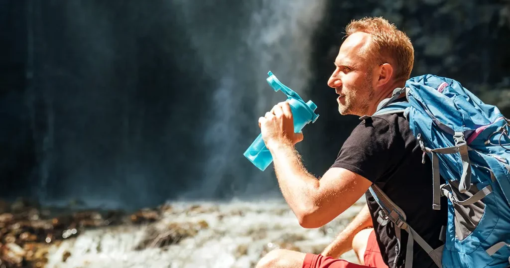 Man with backpack dressed in active trekking clothes drinking the water from touristic flask