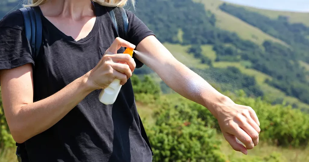 Woman hiker applying Sunscreen spray / sunblock lotion outdoors during summer hike holidays