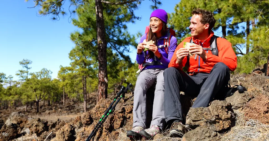 Couple eating lunch taking a break hiking enjoying sandwiches