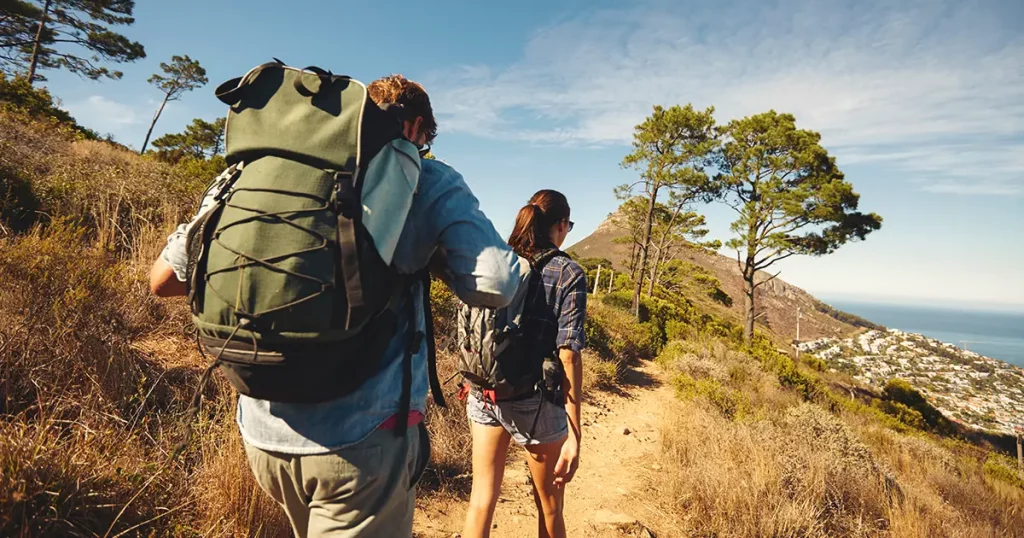 Rear view of two young people walking down the trail path on mountain. Young couple hiking with backpacks.