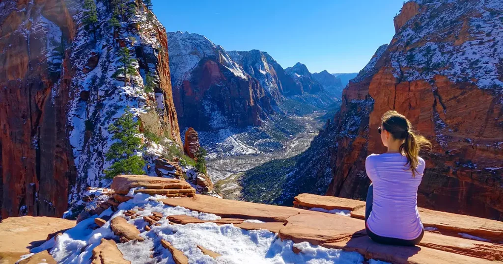 Traveler girl sits and observes the snowy canyon from Angel's Landing