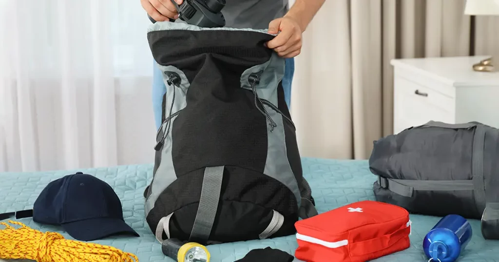 Man packing different camping equipment into backpack at home, closeup