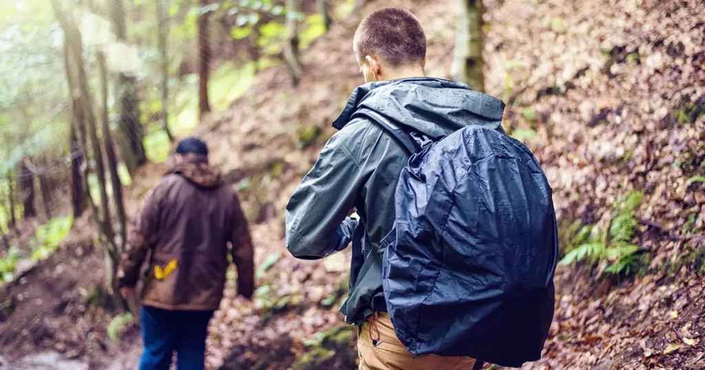 Man with black backpack rain covered hiking in Fagaras Mountains with friends, Romania