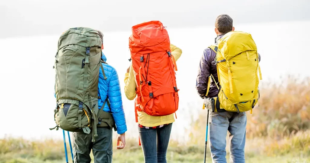 Group of hikers with colorful backpacks standing back near the lake during the foggy weather