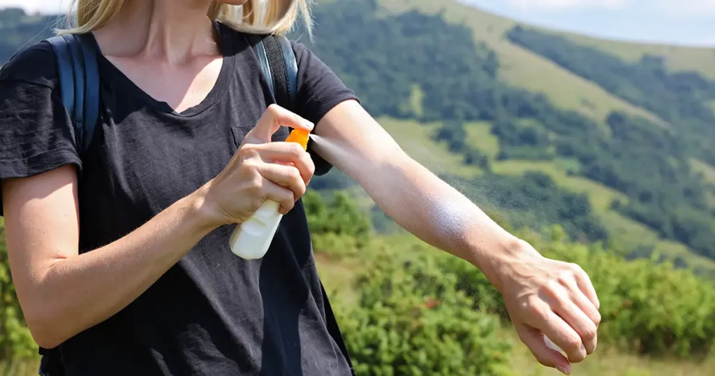 Woman hiker applying Sunscreen spray / sunblock lotion outdoors during summer hike holidays