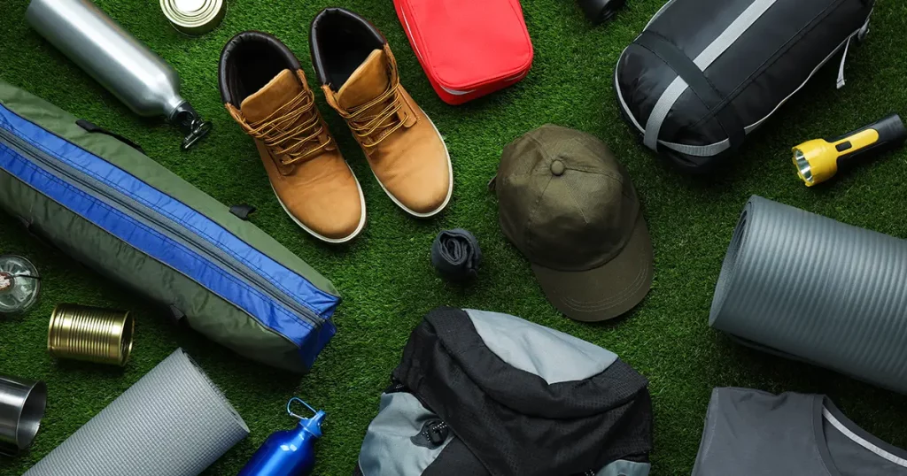 Flat lay composition with different camping equipment on green grass